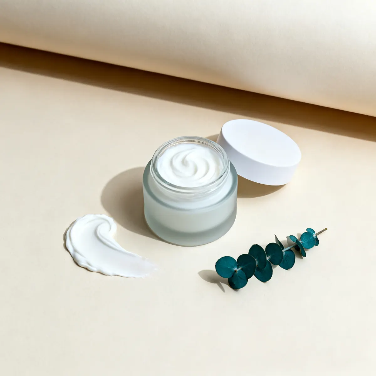 Open cream jar from above, lid set aside, a swatch swirl and a eucalyptus sprig.